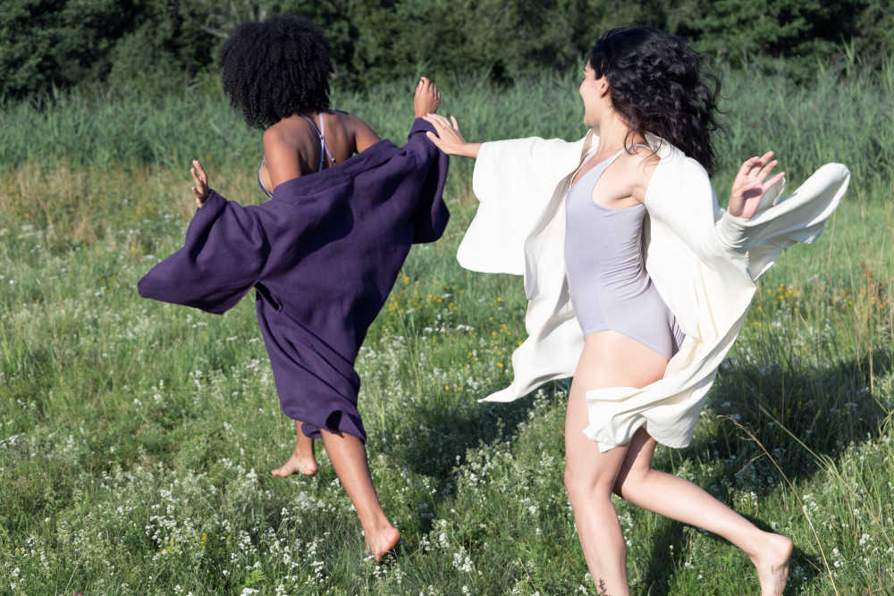 Zwei junge Frauen laufen durch eine Wiese. Sie tragen nachhaltige Lingerie und Kimonos