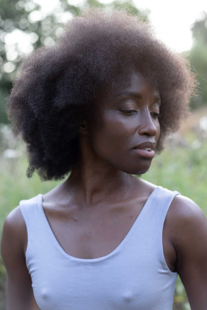 Portrait einer jungen schwarzen Frau. Sie trägt einen nachhaltigen lila Body.